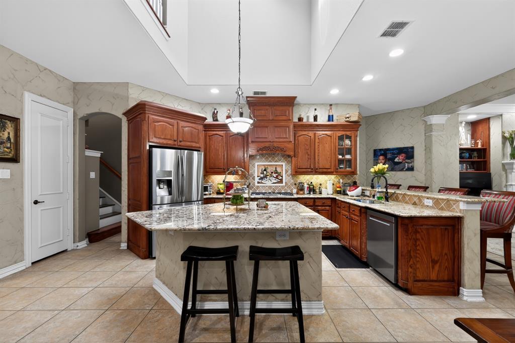 The chef's kitchen at 102 W Carruth Lane with cherry-stained cabinetry, a granite island, gas cooktop, and a soaring two-story ceiling open to a balcony above