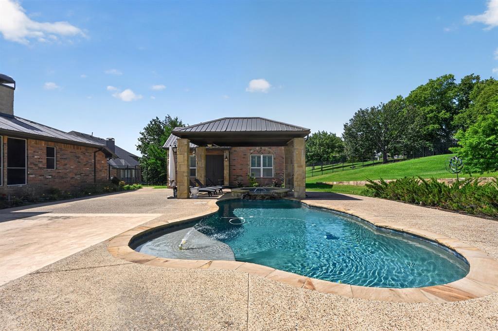 The heated freeform pool at 102 W Carruth Lane with a flagstone deck, fountain jets, and a stone-columned cabana with a metal hip roof behind it