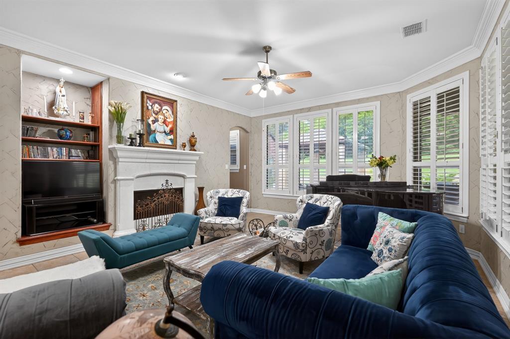 A family room at 102 W Carruth Lane centered on a carved limestone fireplace, with crown molding, textured walls, and plantation-shuttered windows along one side