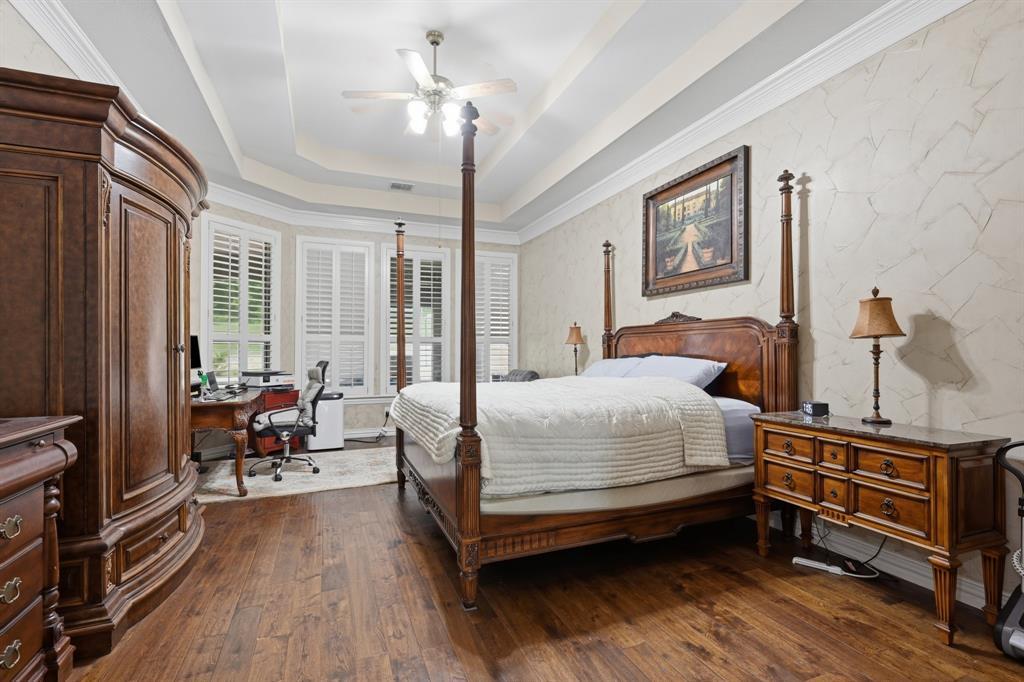 The primary bedroom at 102 W Carruth Lane with a carved four-poster bed, hardwood floors, a stepped tray ceiling, and a wall of plantation-shuttered windows