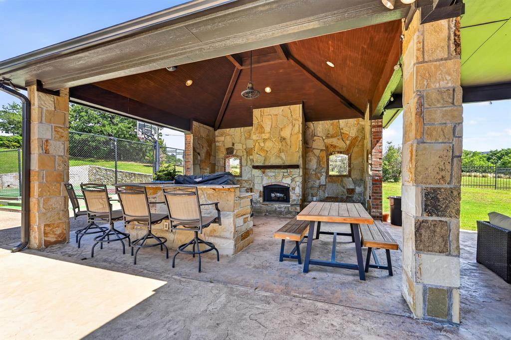 The covered outdoor-kitchen pavilion at 102 W Carruth Lane: a stone bar with seating, a wood-burning stone fireplace, and a vaulted timber ceiling, open to the sport court