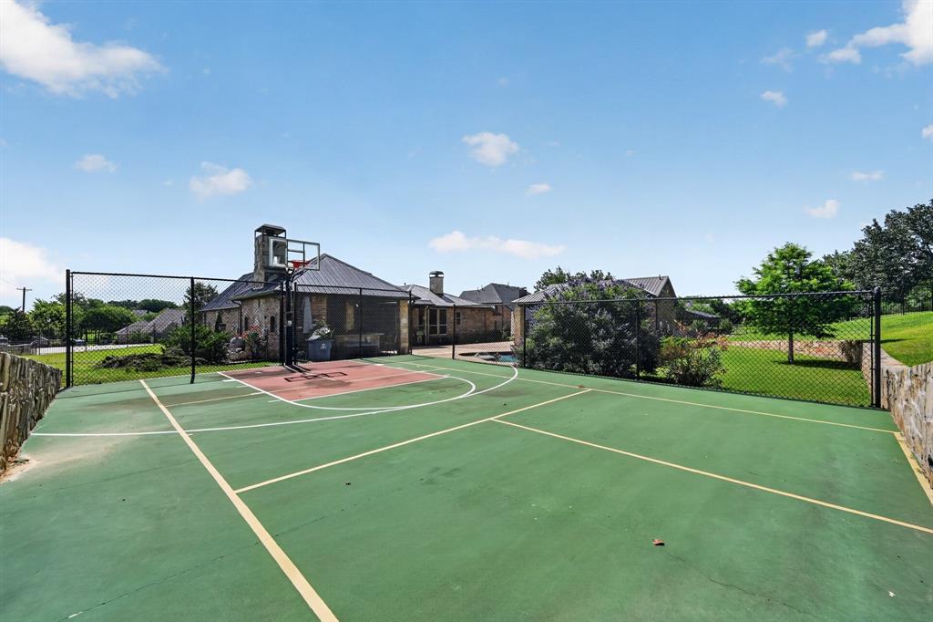 The fenced sport court at 102 W Carruth Lane painted green and red for tennis and basketball, with a hoop at one end and the home and grounds behind it